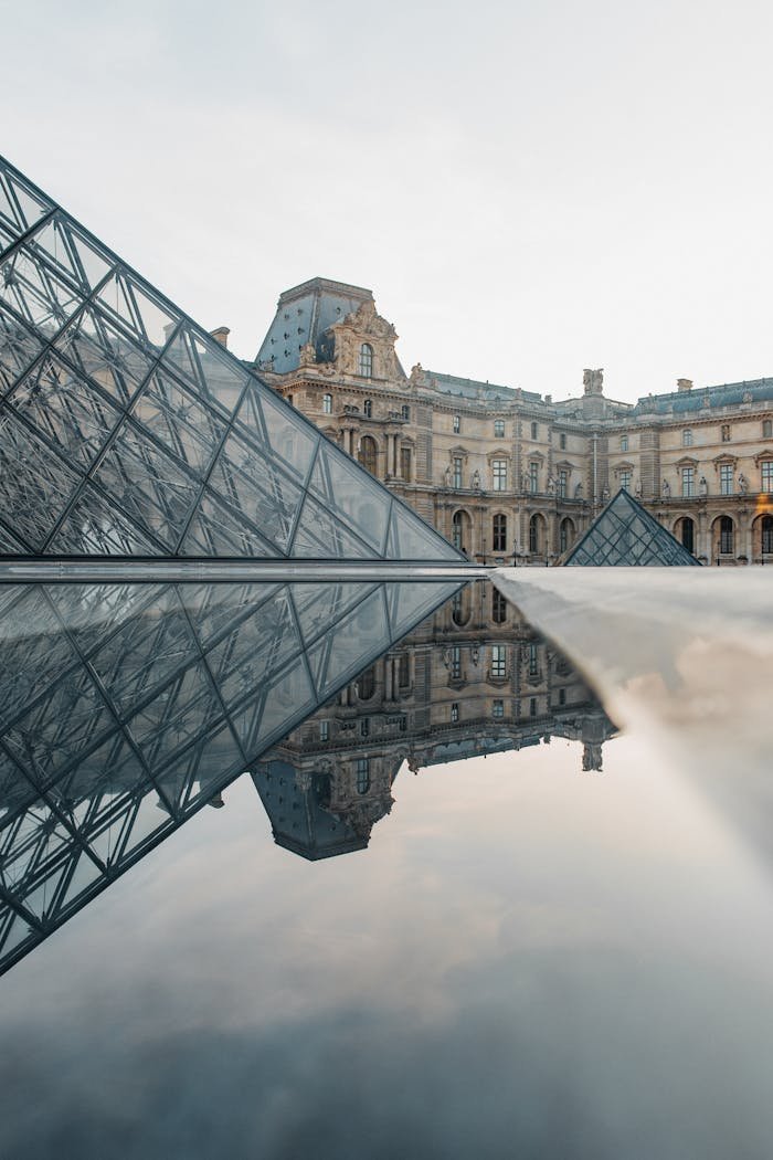 Stunning view of the Louvre Museum and its pyramids reflecting in a puddle at sunset in Paris, France.